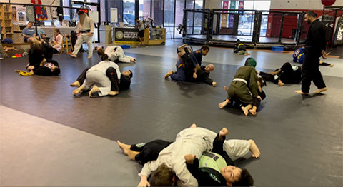 A group of people practicing Brazilian jiu-jitsu on mats inside a training facility.